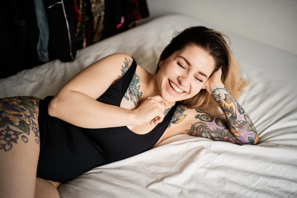 Tatuoitu nainen Viivi Kohtanen makaa sängyllä sivuttain ja nauraa silmät kiinni. Objektiivin Sony FE 35mm f/1.8 testikuva. Valokuva: Anssi Lepikko.